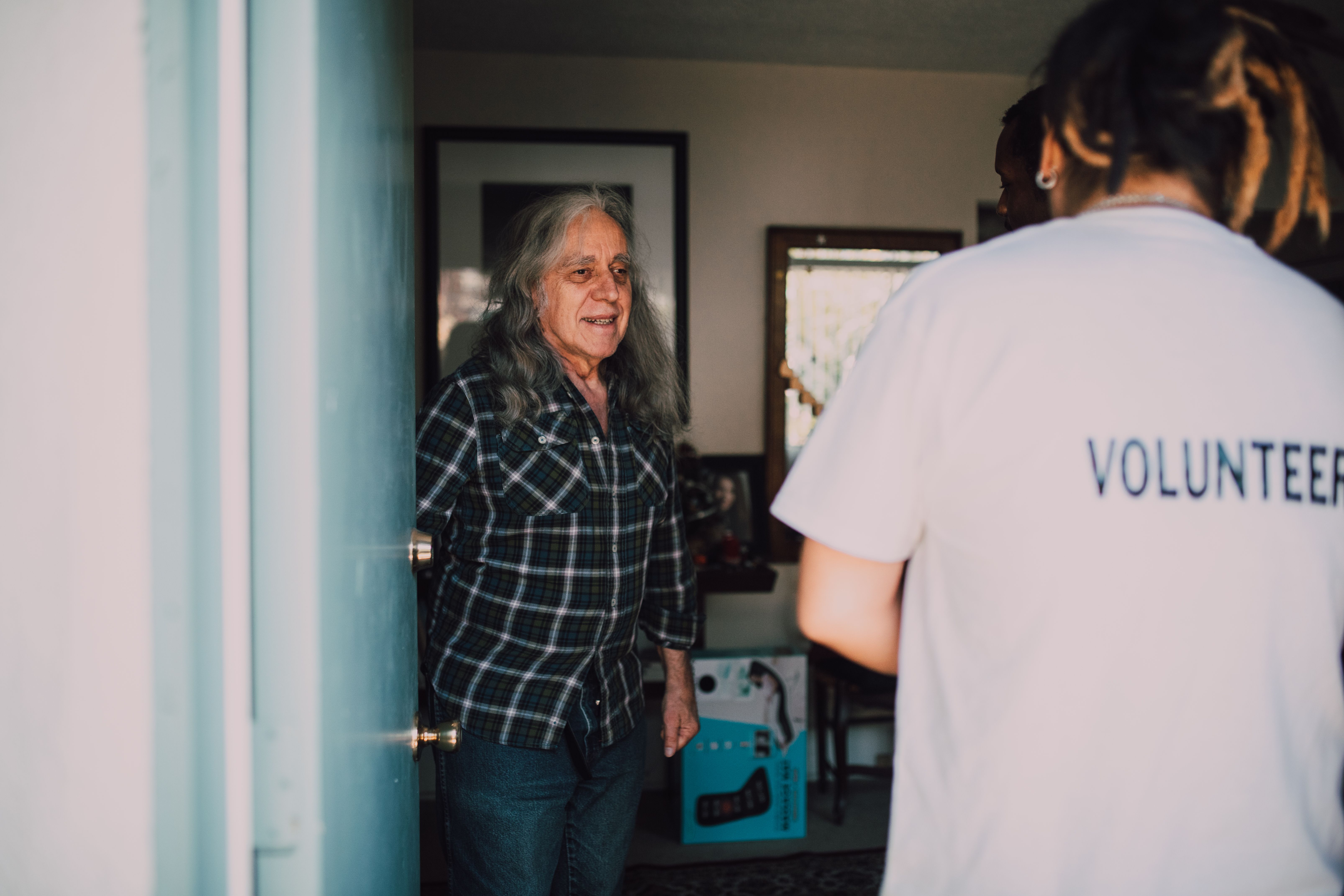 A resident opens the front door to greet two community volunteers.